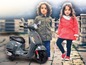 Dwoje dzieci obok szarego skutera Vespa.