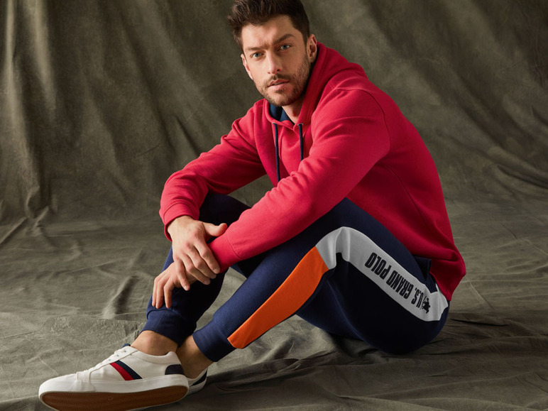 Mężczyzna w czerwonej bluzie i niebieskich spodniach dresowych z logo U.S. Polo Assn.