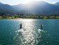 Dwie osoby uprawiają paddleboarding na jeziorze z górami w tle.