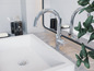 Łazienka z białą umywalką, dwoma chromowanymi bateriami i dozownikiem Le Bain.