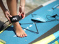 Kobieta przywiązuje leash do swojej nogi na desce SUP Aqua Marina.