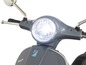 Zbliżenie na przedni reflektor szarego skutera Vespa.