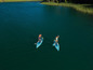 Dwie osoby pływają na dmuchanych paddleboardach na jeziorze.