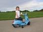 Mała dziewczynka siedzi na niebieskim motorowerze przypominającym Vespę.
