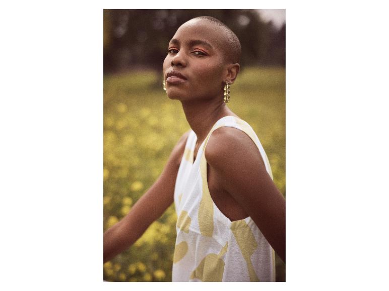 Modelka w sukience bez rękawów z abstrakcyjnym wzorem na polu żółtych kwiatów.