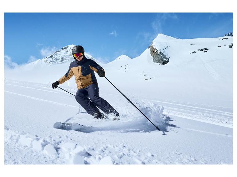 Narciarze w niebieskich spodniach i brązowej kurtce zjeżdża na nartach po stoku.