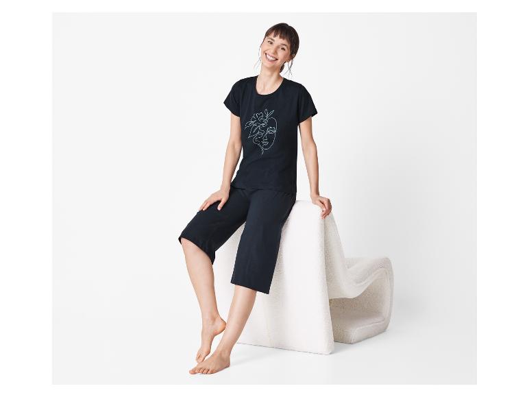 Kobieta w czarnej piżamie z nadrukiem siedzi na białym pufie.