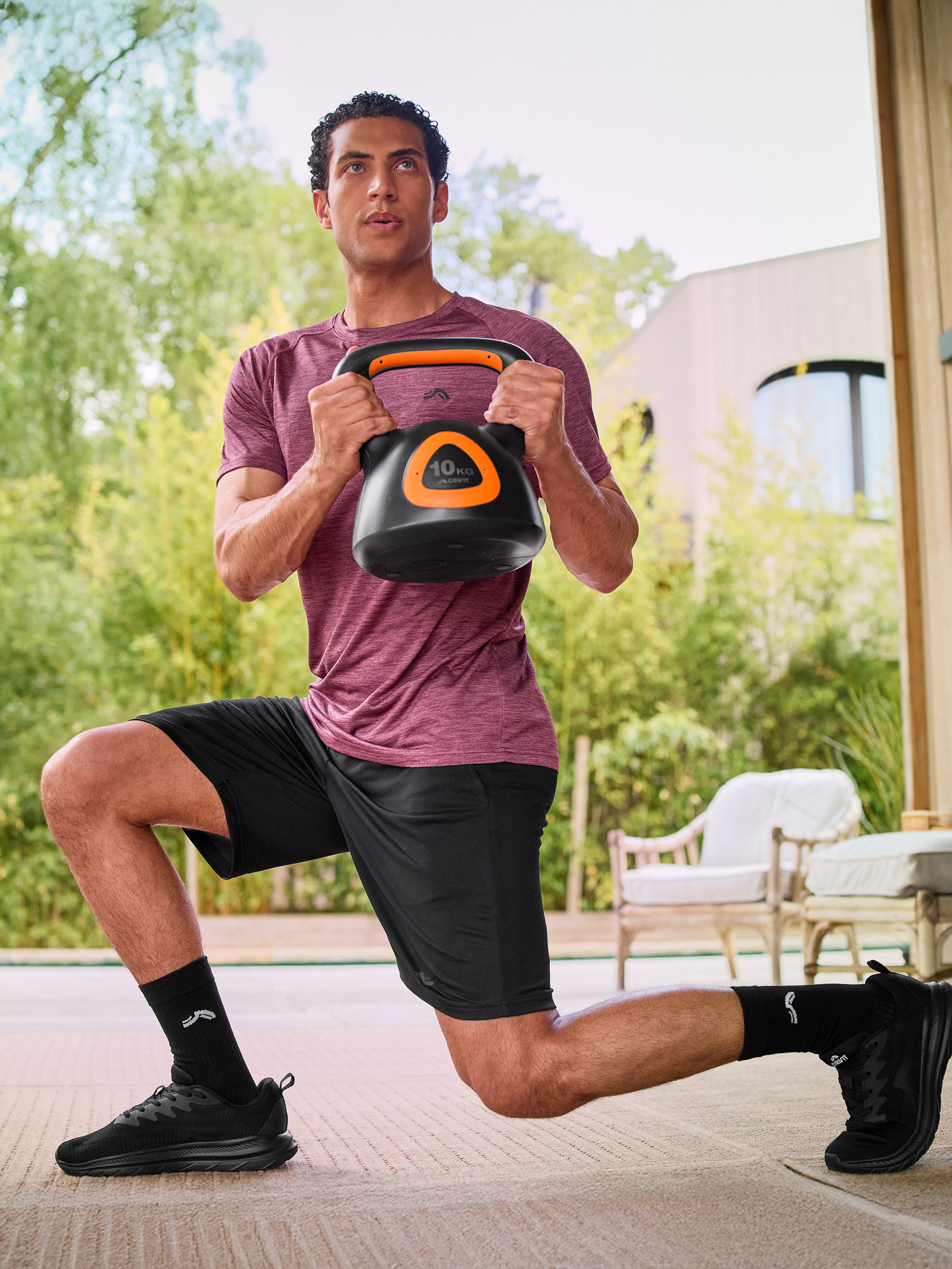 Mężczyzna w sportowym stroju wykonujący wykrok z czarnym kettlebell 10 kg.