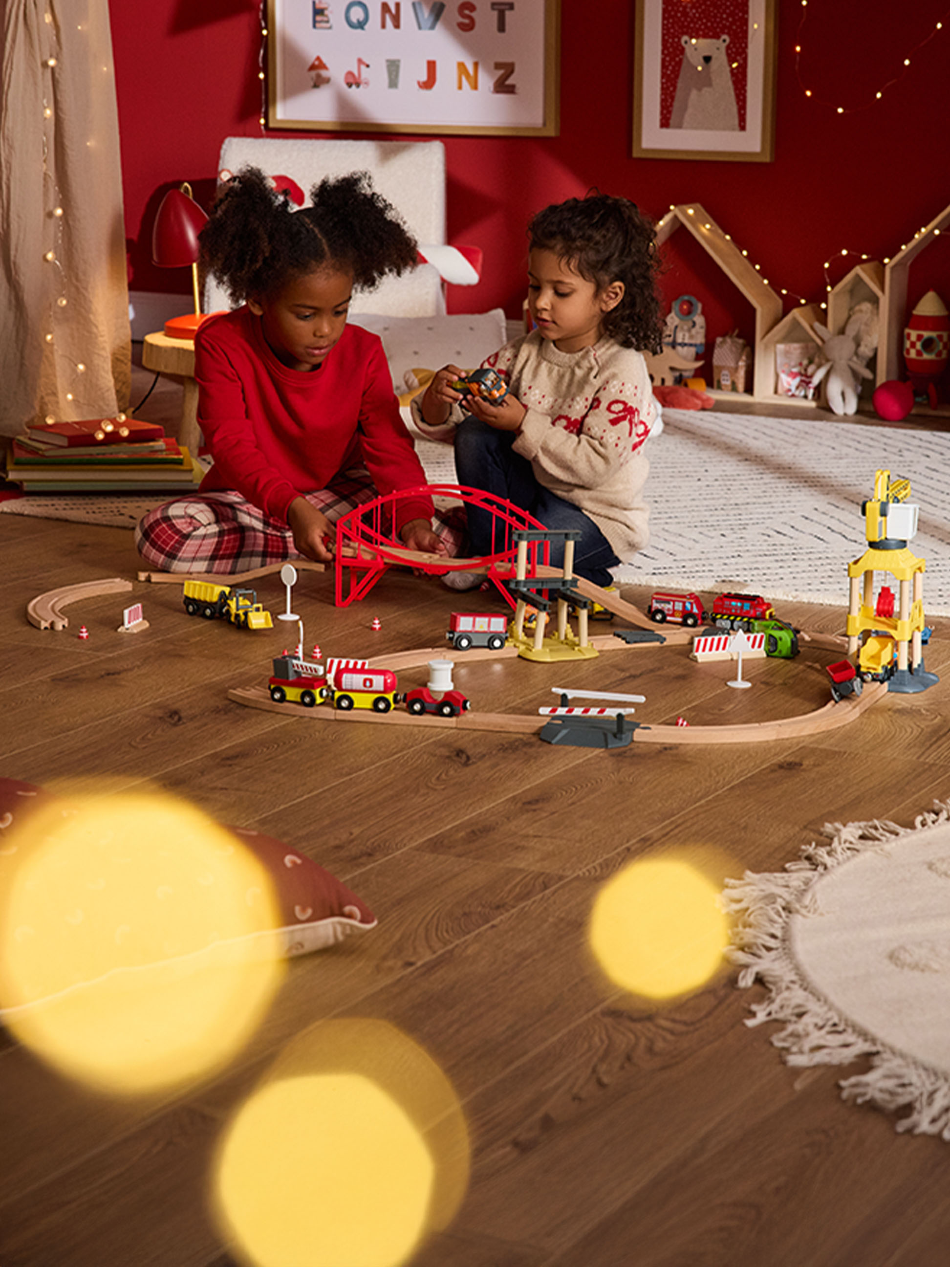 Dwoje dzieci bawi się drewnianym zestawem kolejowym i pojazdami na drewnianej podłodze.