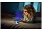 Uśmiechnięta dziewczynka w łóżku z projektorem lampki nocnej wyświetlającym gwiazdy i księżyc.