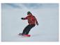 Snowboardzista w czerwonej kurtce we wzory i czarnych spodniach, na czerwonej desce snowboardowej.
