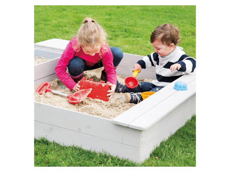 Dwoje dzieci bawi się w drewnianej piaskownicy.