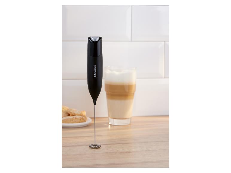 Czarny spieniacz do mleka na drewnianej powierzchni obok szklanki latte i ciastek