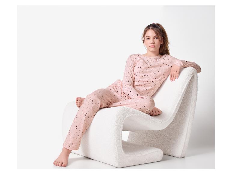 Młoda kobieta siedząca na białym krześle, ubrana w różową piżamę w kropki.
