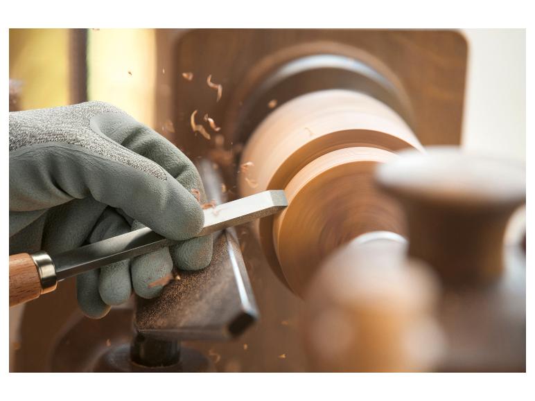 Ręka w rękawiczce używa dłuta do obróbki drewnianego dysku na tokarce.