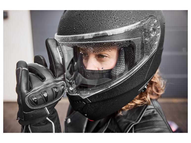 Osoba w czarnym kasku motocyklowym z kroplami wody i czarną rękawicą z napisem 'VISOR WIPE'.
