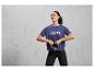 Kobieta w niebieskiej koszulce sportowej z napisem 'Break the Limits' trzyma czarną kettlebell.