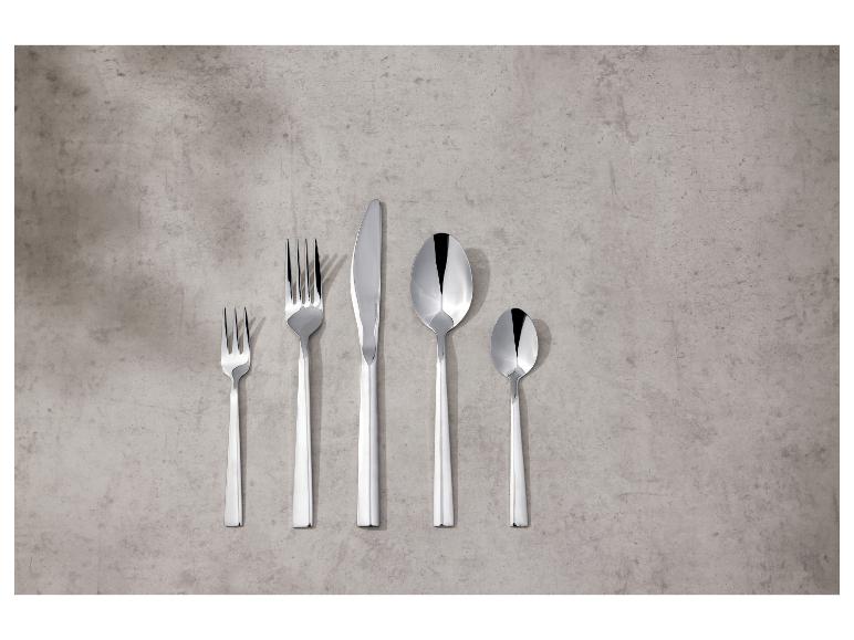 Zestaw błyszczących, srebrnych sztućców na betonowym tle.