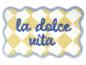 Żółto-biała kraciasta mata łazienkowa z niebieskim napisem „la dolce vita”.