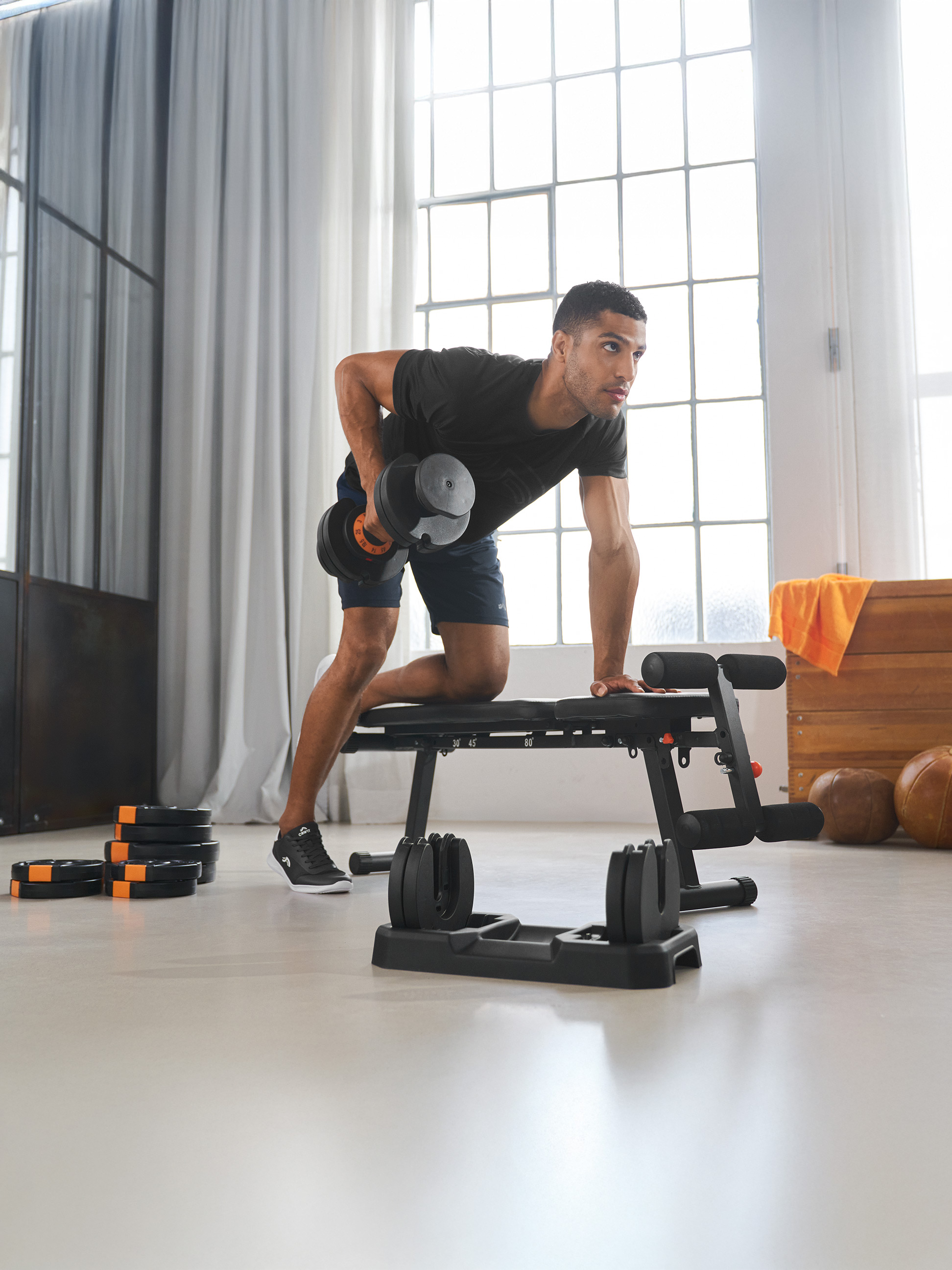 Mężczyzna ćwiczy z regulowanym hantlem i ławką do ćwiczeń w jasnym pokoju.