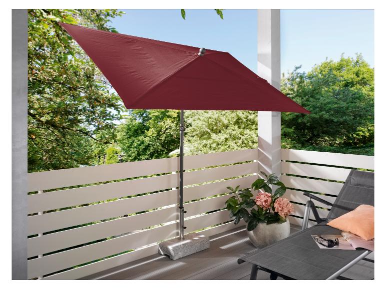 Czerwony parasol na balkonie z leżakiem i roślinami.