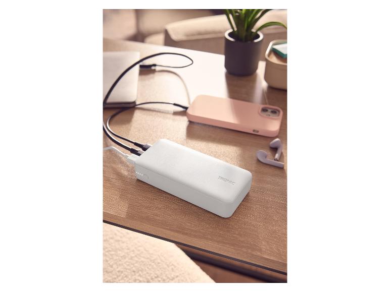 Biały power bank ładujący laptopa i smartfon na drewnianym stole.