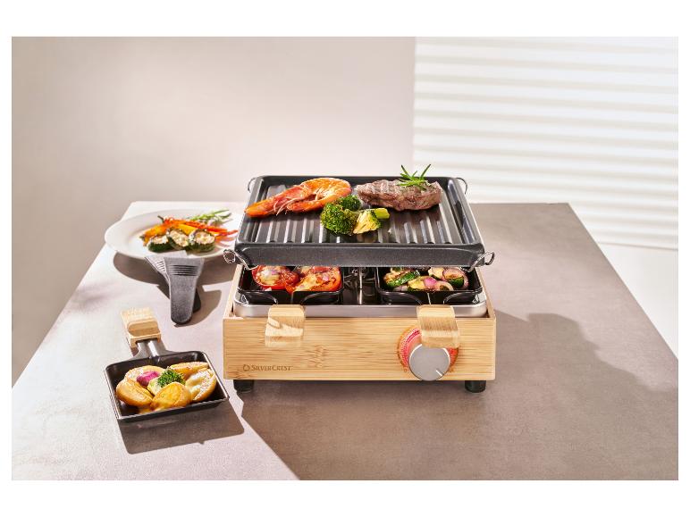 Bambusowy grill raclette z mięsem, krewetkami i warzywami na grillu i w patelniach.