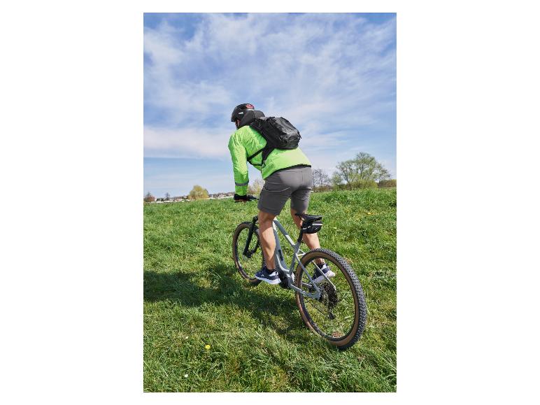 Rowerzysta z plecakiem i zieloną koszulką rowerową na rowerze górskim na trawiastym polu.