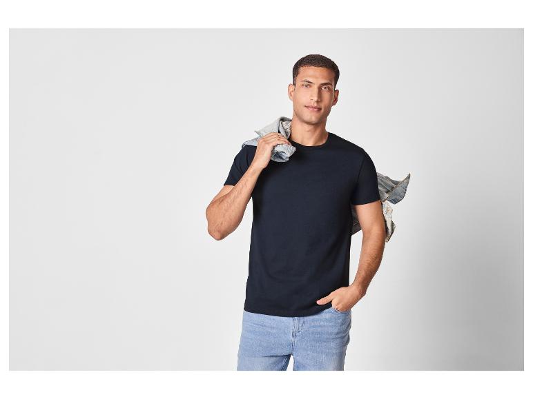 Mężczyzna w czarnym t-shircie i jasnoniebieskich dżinsach, z kurtką dżinsową na ramieniu.