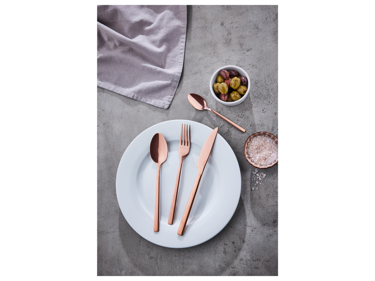 Widelec, nóż i łyżka ze stali nierdzewnej w miedzianym kolorze na białym talerzu.