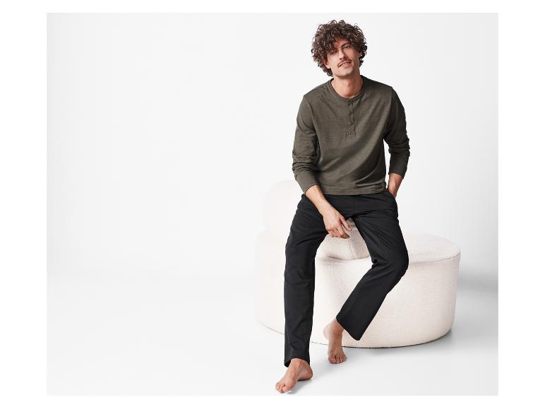 Mężczyzna z kręconymi włosami pozuje w ciemnozielonej i czarnej piżamie.