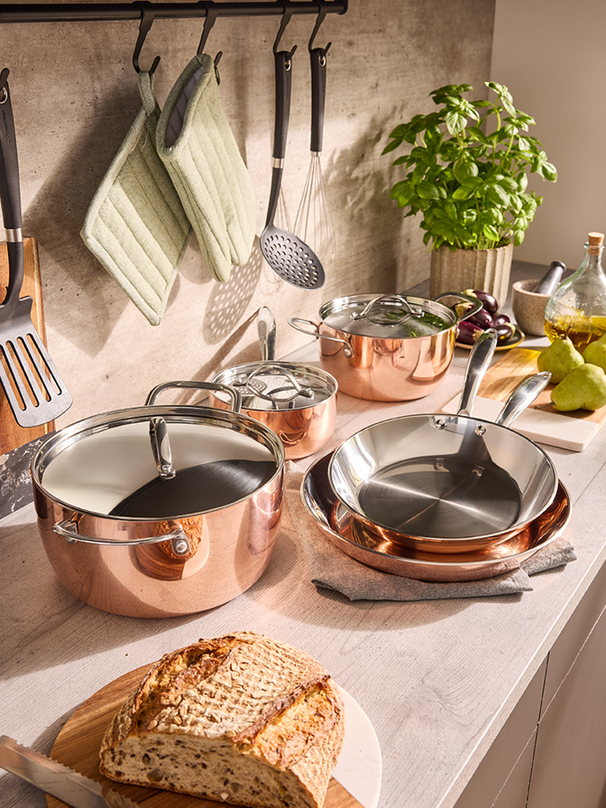 Zestaw miedzianych garnków i patelni na blacie kuchennym, z chlebem i ziołami.