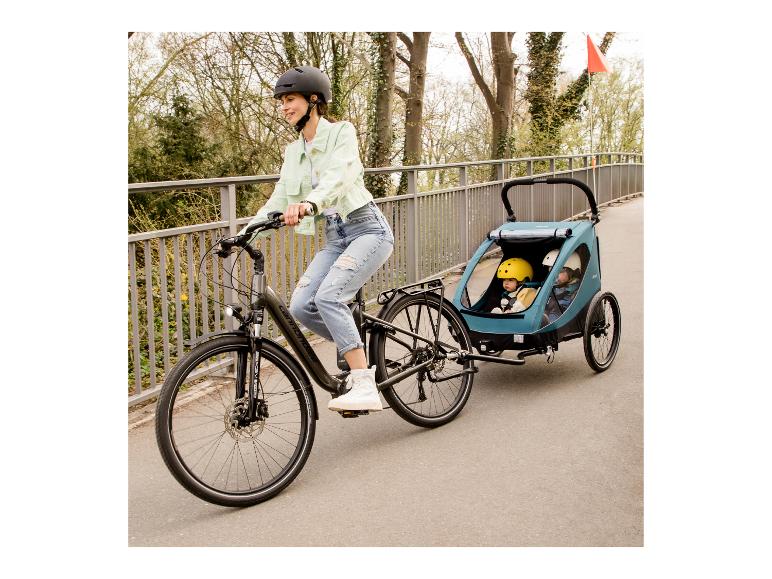Kobieta na rowerze elektrycznym ciągnie przyczepkę rowerową z dwójką dzieci.