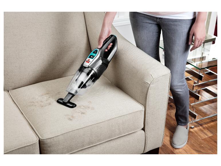 Kobieta czyści materiałową sofę odkurzaczem ręcznym Bissell