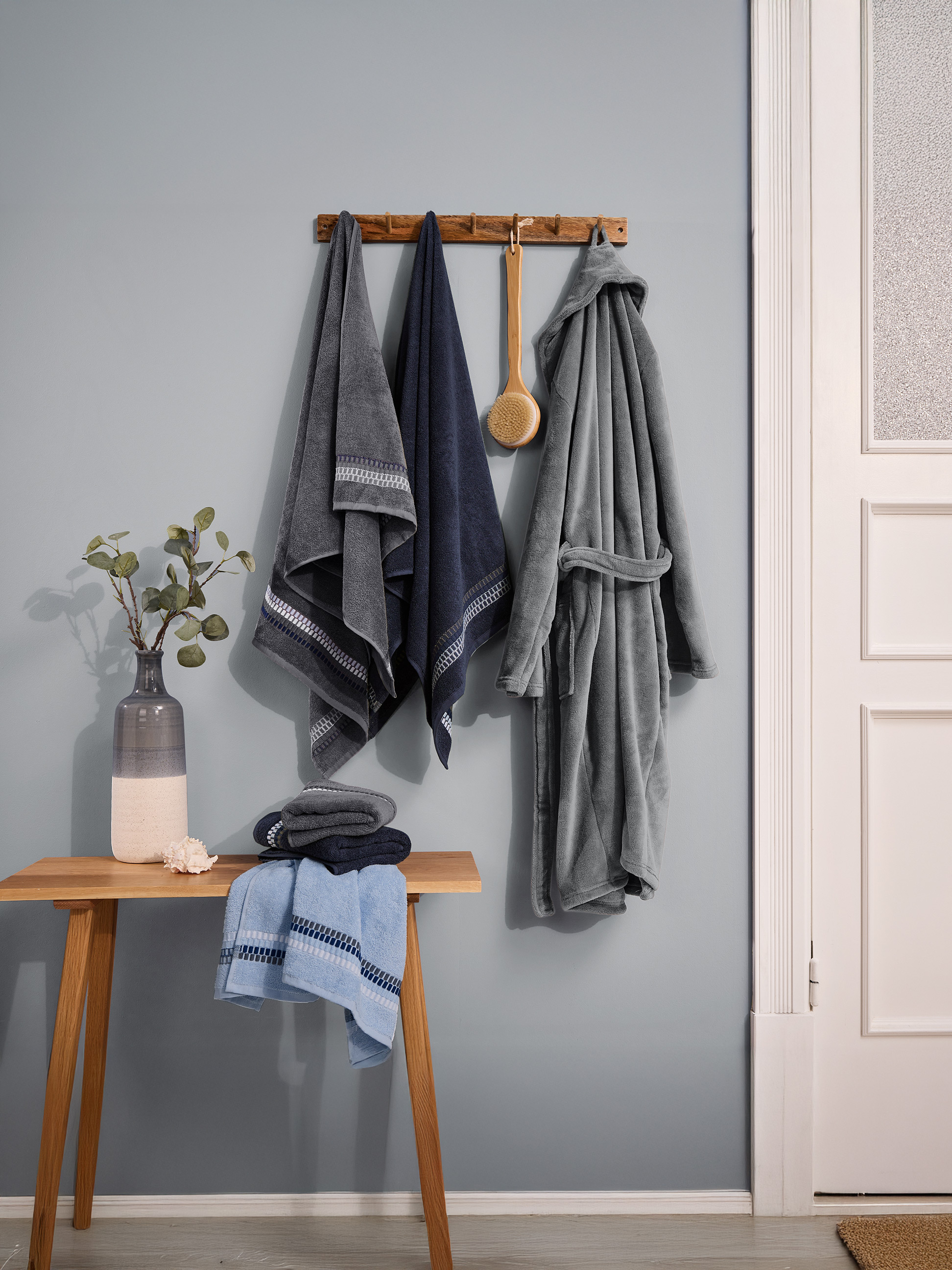 Ręczniki i szlafrok w odcieniach niebieskiego i szarości, wiszące na ścianie.
