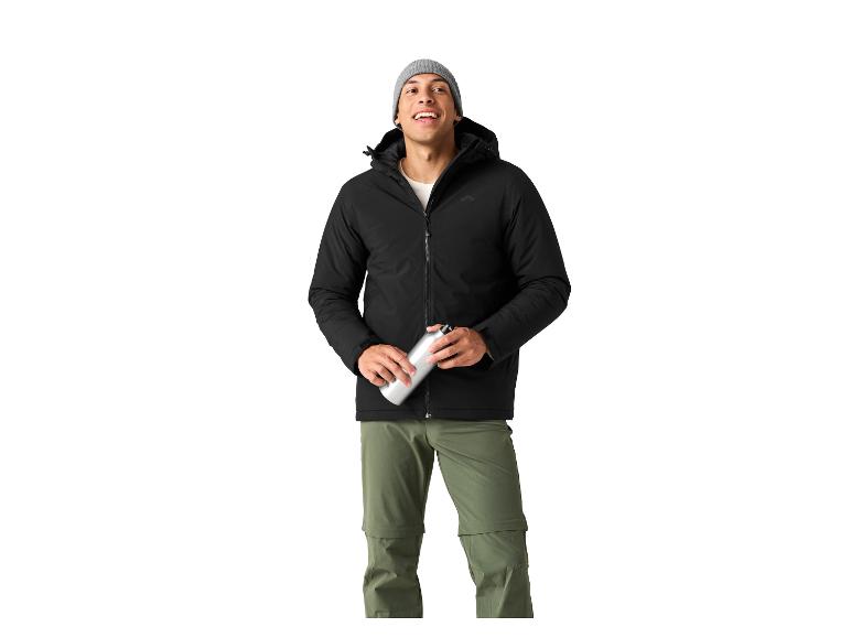 Uśmiechnięty mężczyzna w czarnej kurtce i spodniach khaki, trzymający butelkę wody.