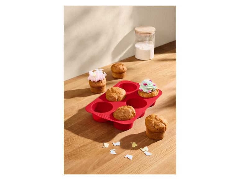 Czerwona silikonowa forma do muffinek z babeczkami, niektóre ozdobione lukrem.