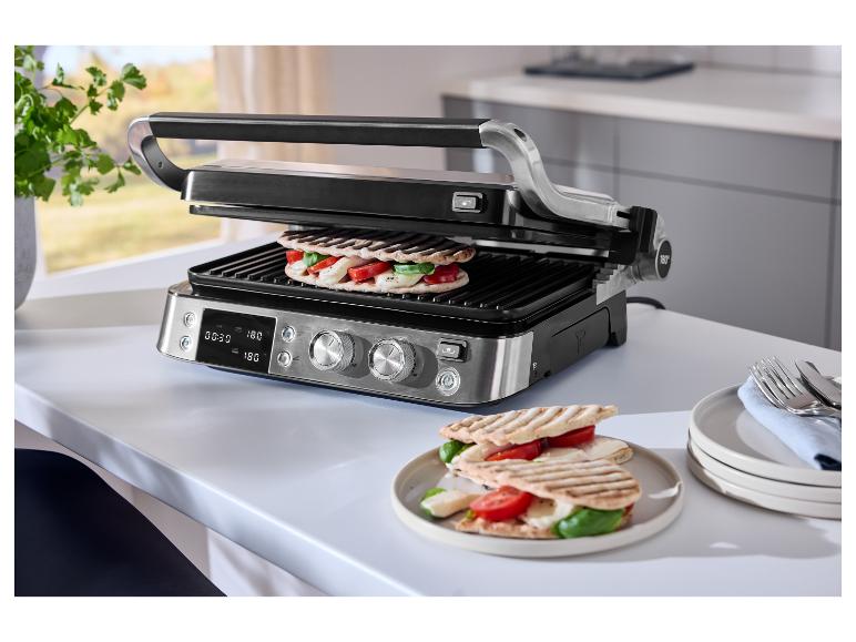 Grill z dwoma kanapkami, pomidorami, mozzarellą i bazylią, na białym stole.