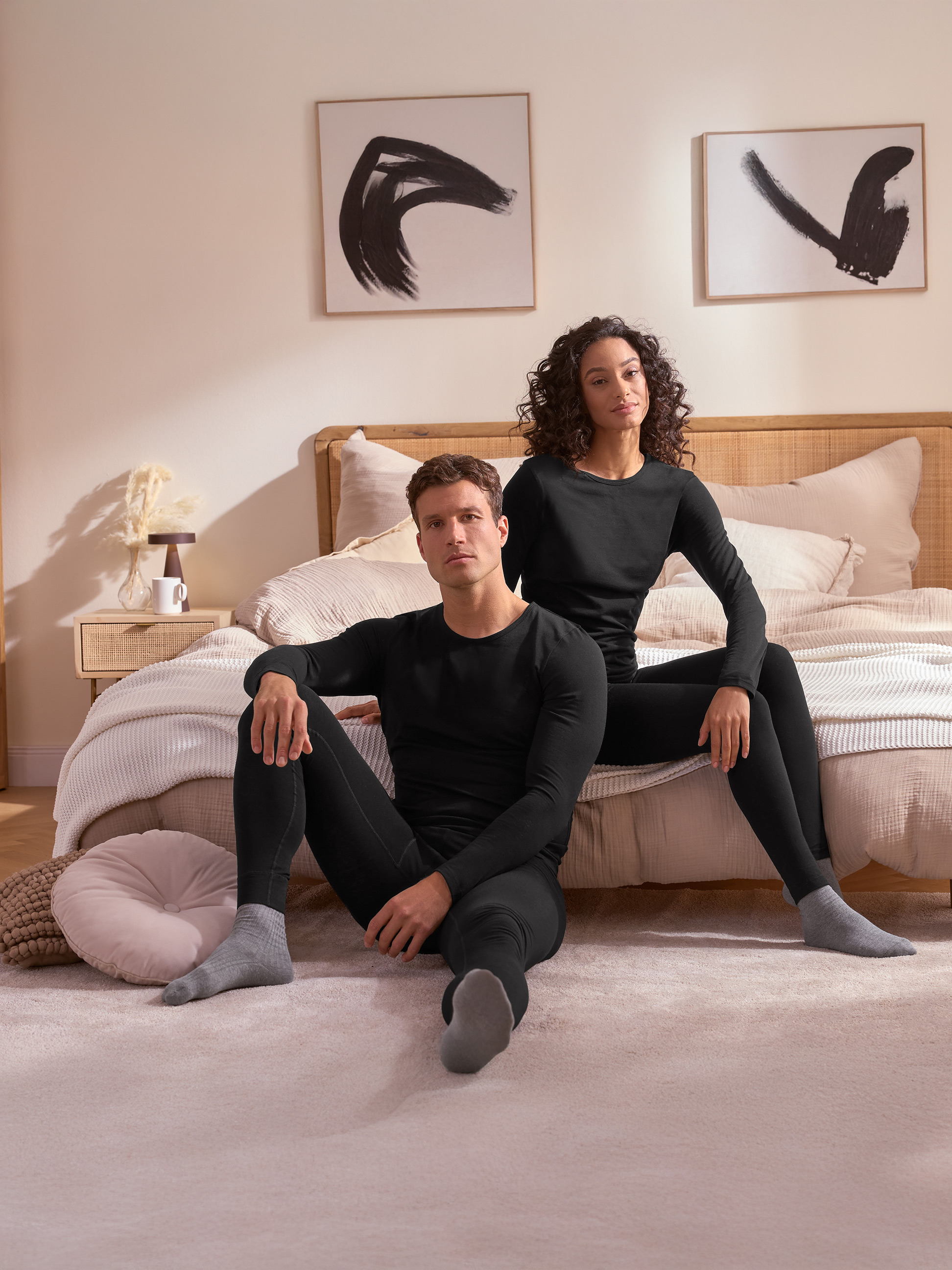 Para w czarnej bieliźnie termicznej siedzi na podłodze przed łóżkiem.