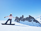 Snowboardzista w różowym ubraniu i niebieskich okularach sunie na snowboardzie po zasneżonym stoku.