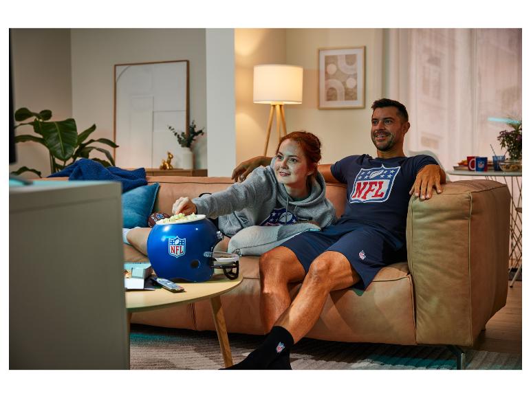 Para ogląda telewizję na kanapie z popcorn w kubku w kształcie kasku NFL.