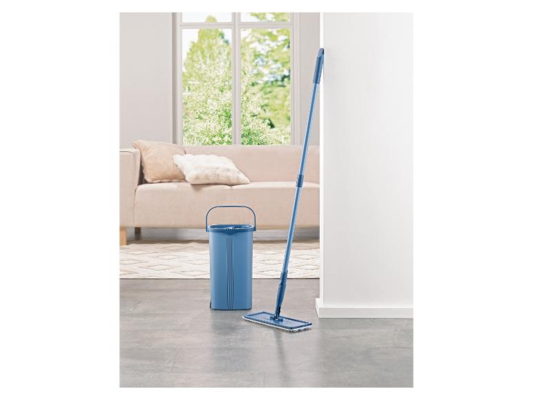 Niebieskie wiadro i mop w jasnym salonie z sofą i oknem.
