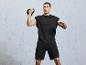 Mężczyzna w czarnej koszulce i spodenkach  wykonuje ćwiczenie z odważnikiem kettlebell.