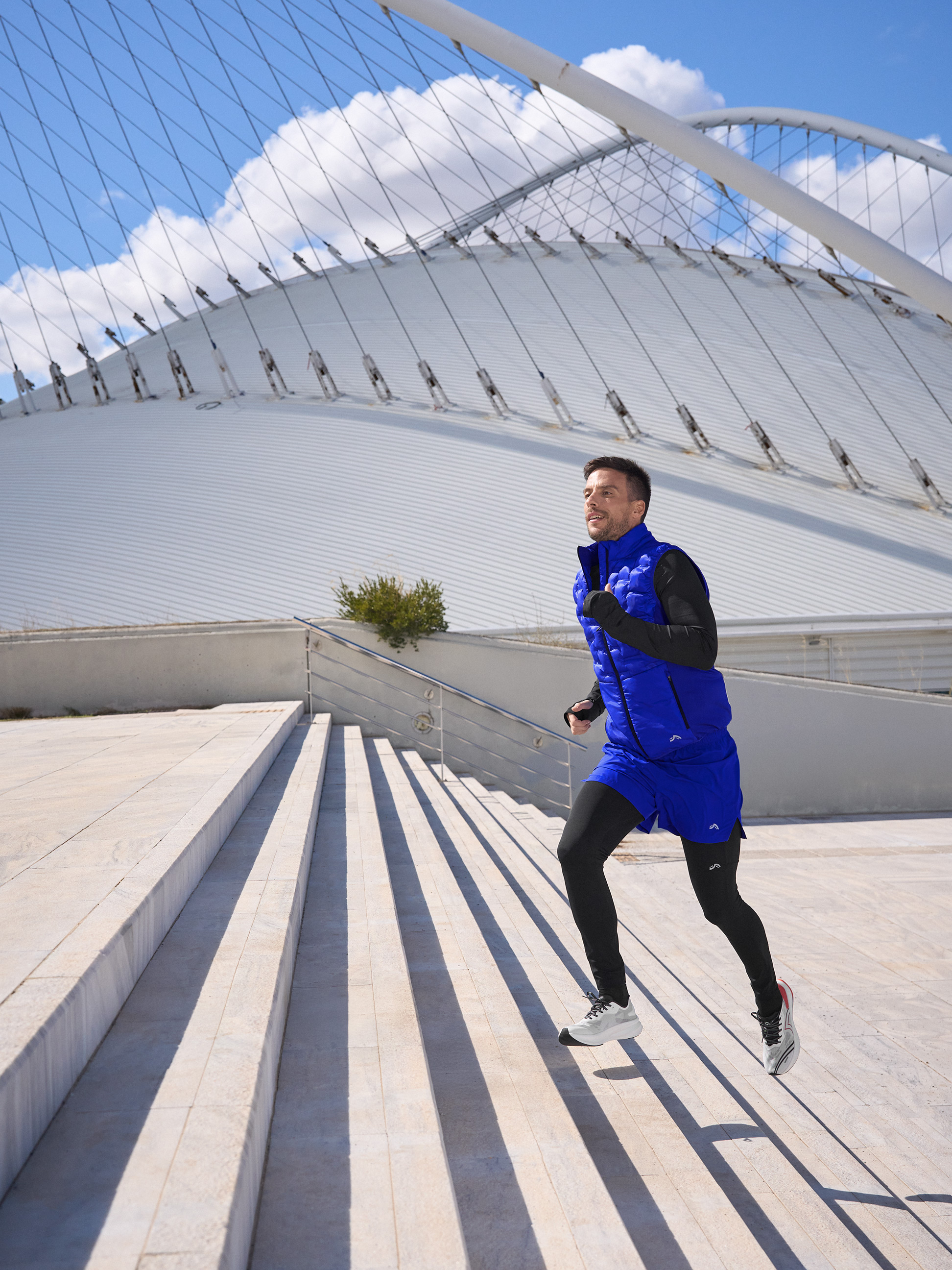 Mężczyzna w niebieskiej kamizelce do biegania i czarnych legginsach biegnie po schodach.
