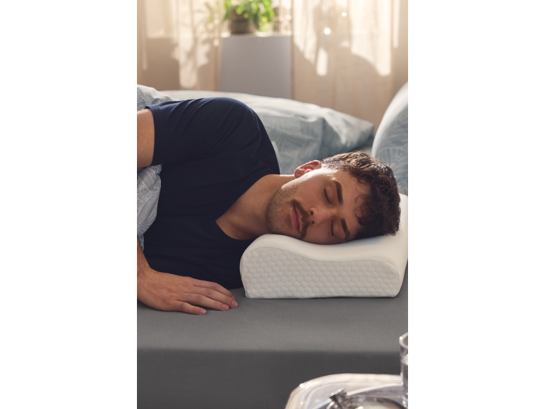 Mężczyzna śpiący na boku na szarej pościeli, z głową na ergonomicznej poduszce.