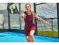 Kobieta w bordowej sukience sportowej gra w padla z rakietą i piłką.