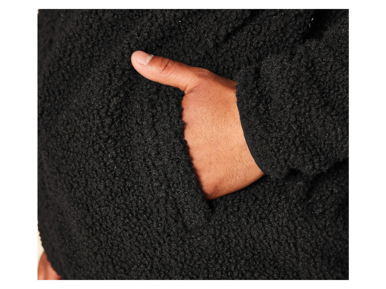 Zbliżenie na czarną kurtkę z polaru z ręką w kieszeni.