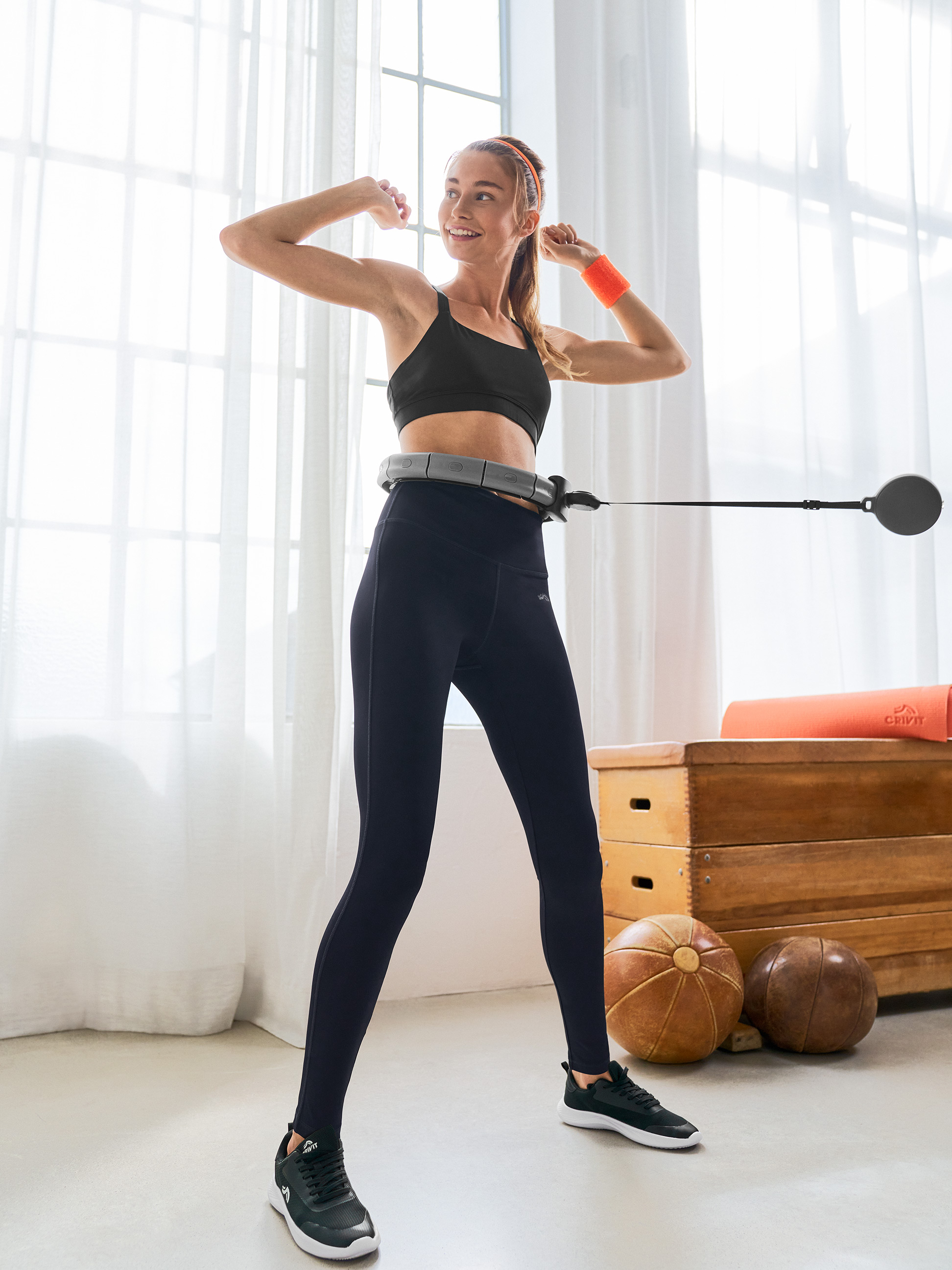 Kobieta w biustonoszu sportowym i legginsach Crivit używająca inteligentnego hula-hoopu