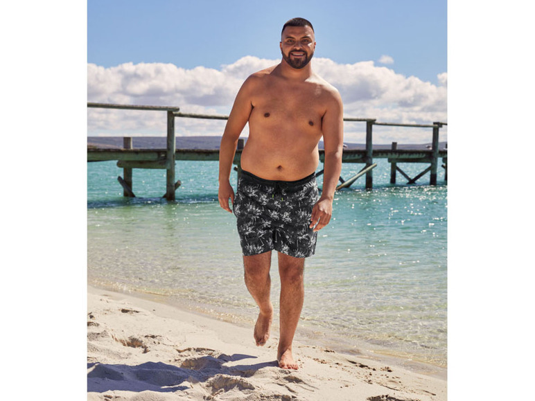 Mężczyzna w kąpielówkach z palmowym wzorem na plaży.