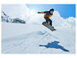 Snowboardzista w niebieskiej kurtce i czarnym kasku skacze nad śniegiem.
